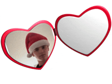 a boy wearing a santa hat is reflected in two heart shaped mirrors