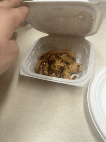 a person is holding a plastic container of food with a plate in the background