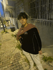 a young man is smoking a cigarette on a sidewalk in front of a building .