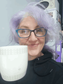 a woman with purple hair and blue glasses holds a white cup