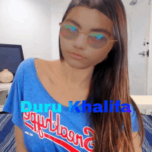 a woman wearing sunglasses and a blue shirt that says guru khalifa on it