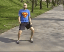 a man in a blue superman shirt is dancing on a sidewalk .