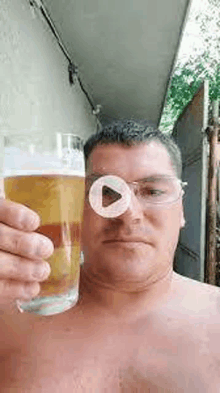 a shirtless man is holding a glass of beer in front of his eye .