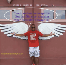 a man in a red shirt stands in front of a mural of angel wings