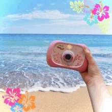 a person is holding a pink vtech camera in front of the ocean