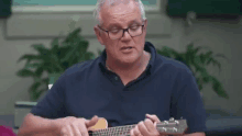 a man wearing glasses is playing an acoustic guitar in a room .