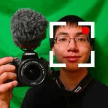 a man is holding a camera and a microphone in front of a green screen .