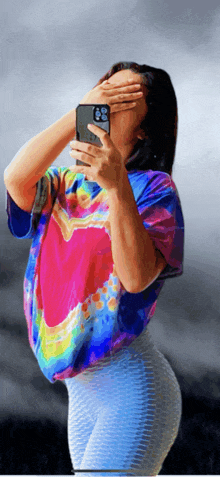 a woman in a tie dye shirt is taking a selfie