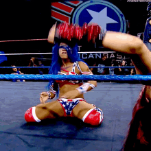 a woman in a patriotic outfit is kneeling down in a wrestling ring with a sign that says american on it