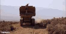 a man stands on top of a dump truck in a desert with the word tremors on the bottom right