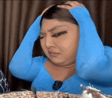 a woman in a blue shirt is holding her head while sitting at a table with a plate of food .