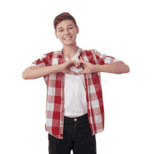 a young boy in a red and white plaid shirt is making a heart shape with his hands