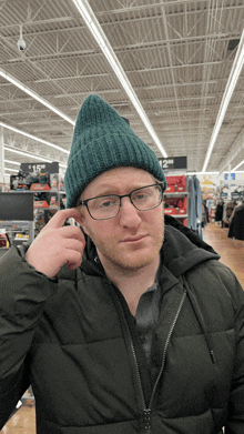 a man wearing glasses and a green beanie is standing in front of a sign that says $ 12