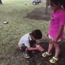 a little girl in a pink shirt is standing next to a little boy kneeling down in the grass .