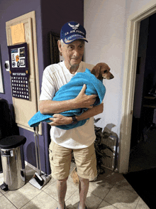 a man wearing a u.s. air force hat is holding a small dog wrapped in a blue towel