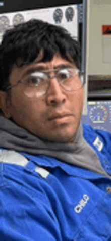 a man wearing glasses and a blue jacket is sitting in front of a computer monitor .