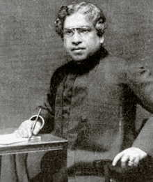 a black and white photo of a man sitting at a table holding a pen .