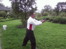 a man in a white shirt and black pants is holding a gun in a garden