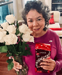 a woman holding a bouquet of white roses and a bag of lindor milk chocolate