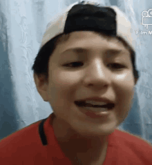 a young boy wearing a baseball cap and a red shirt is smiling for the camera