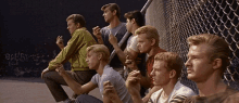 a group of young men sit in front of a chain link fence with graffiti on the wall that says borg