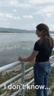 a woman leaning on a railing overlooking a body of water with the words " i don 't know " written below her