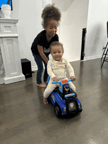 a little girl pushes a baby on a toy car with paw patrol on the back