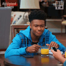 a young man is sitting at a table with a glass of orange juice and a phone in front of him