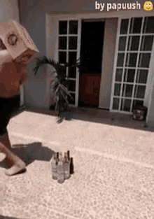 a man wearing a paper bag on his head is standing next to bottles of alcohol on the ground .