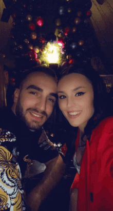 a man and a woman pose for a photo in front of a christmas tree