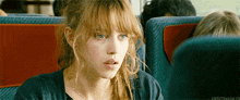 a woman with blonde hair and blue eyes is sitting on a bus .