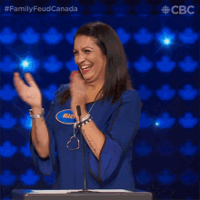 a woman in a blue shirt is applauding in front of a podium with a cbc logo in the corner