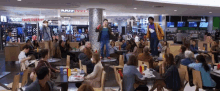 a group of people sitting at tables in a food court with a kid 's foot locker store in the background