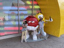 two young girls standing next to a statue of a red m & m