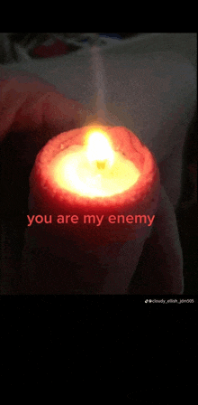 a person is holding a lit candle that says " you are my enemy " on it