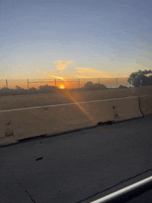 the sun is setting over a highway barrier