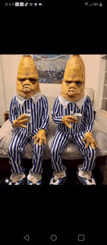 two bananas in pajamas are sitting on a bed holding cups of coffee