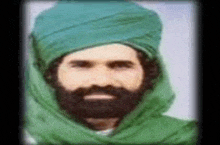 a man with a beard and a green turban is wearing a green scarf .