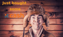 a man wearing a fur hat is smiling in front of a wooden wall with just bought some cash written on it