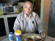 an elderly man sitting at a table with a can of light star beer