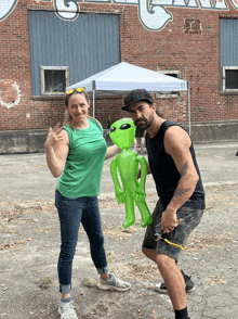 a man and a woman are posing for a picture with an inflatable green alien