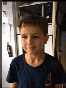 a young boy standing in front of a microwave that says 13:53 on it