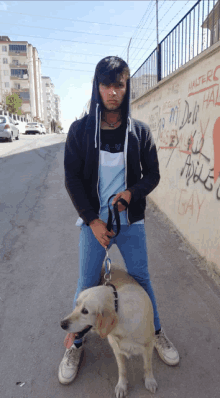 a young man standing next to a dog with graffiti on the wall behind him that says gay