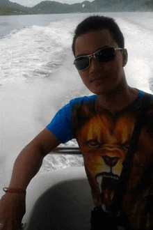 a man wearing sunglasses and a shirt with a lion on it is sitting on a boat