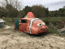 a car painted to look like a clown fish is parked in a dirt field .