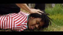 a man in a red and white striped shirt is laying on the grass with his head on someone 's lap .