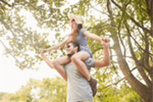 a man is carrying a girl on his shoulders in a park .