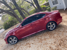 a red car is parked in front of a house with trees in the background