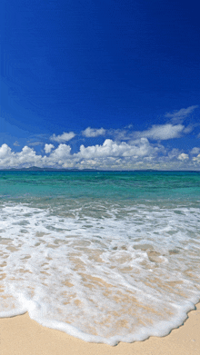 a sandy beach with a blue sky and white clouds