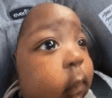 a close up of a baby 's face with a stroller in the background .